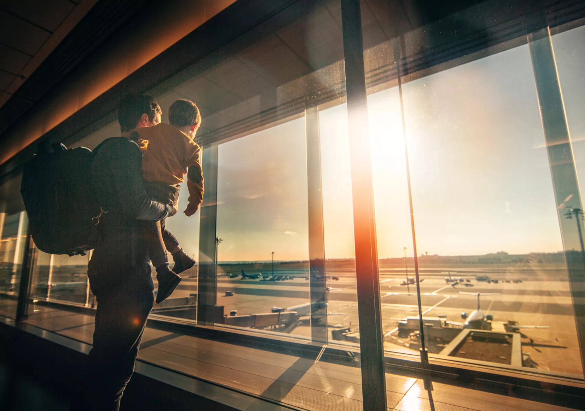 Father and young son watching planes on the tarmac inside a passenger terminal,