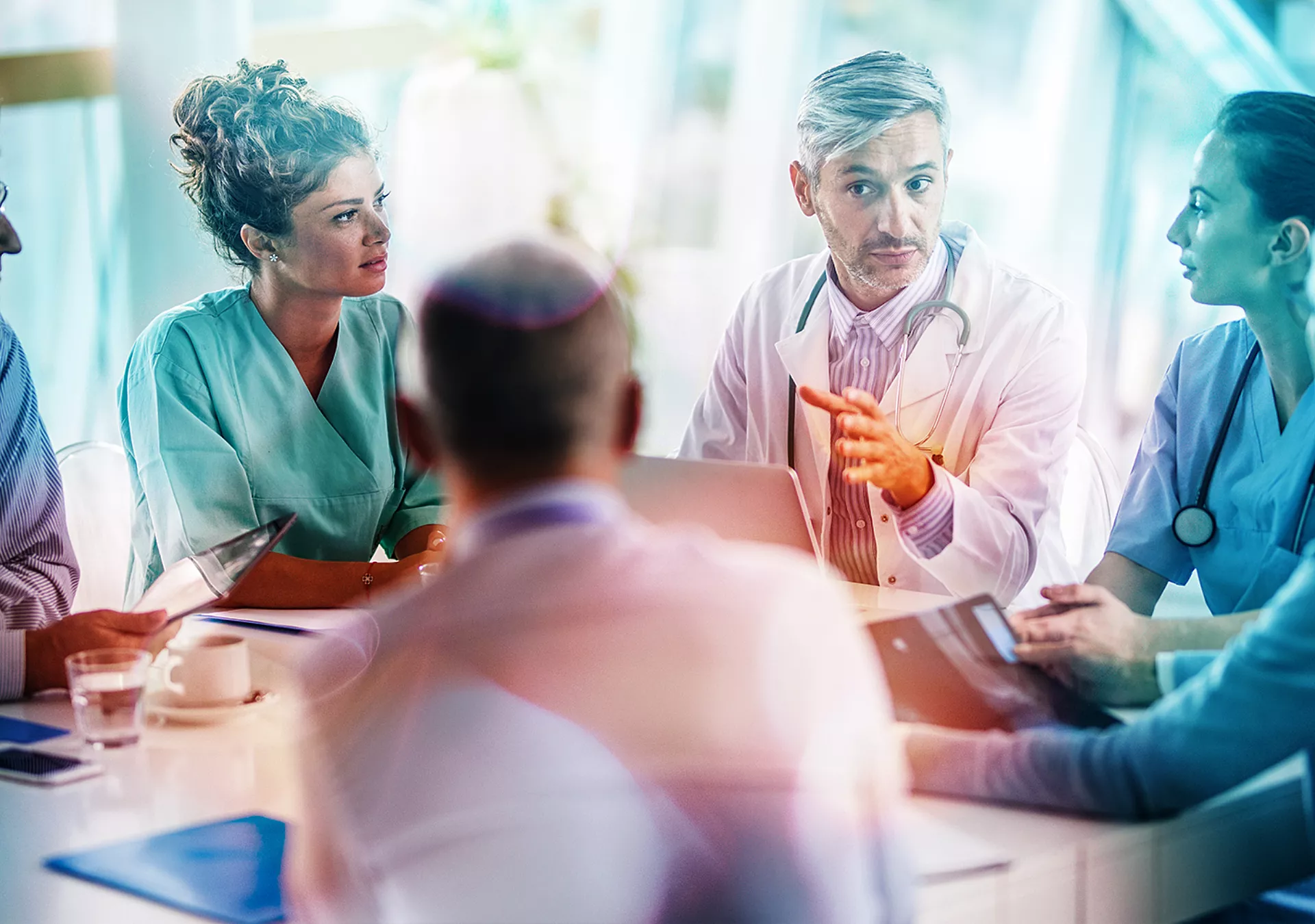 Male doctor and his female colleagues talking to team of business people at a meeting