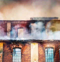 Photo of a burning old red-brick factory with a lot of smoke.