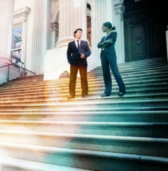 A well dressed man and woman converse on the steps of a legal or municipal building.
