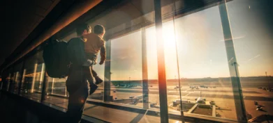Father and young son watching planes on the tarmac inside a passenger terminal,