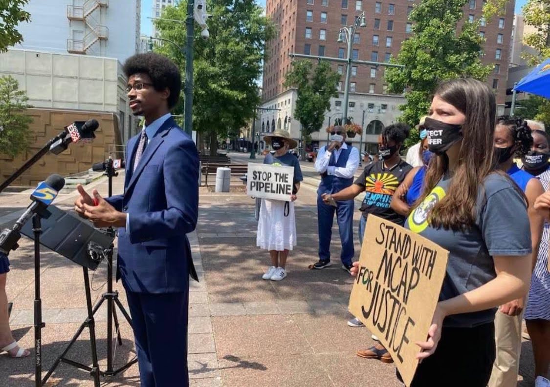A photo of Justin speaking into microphones surrounded by activists protesting the Byhalia oil pipeline.