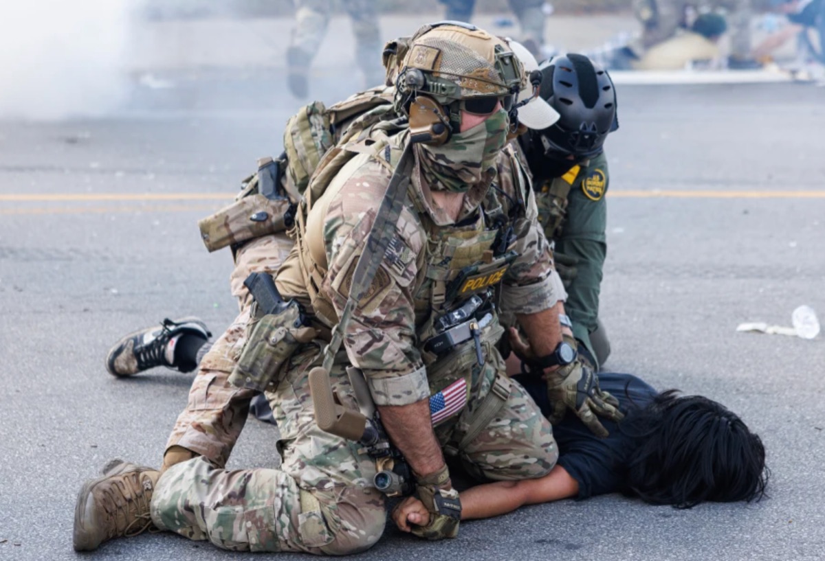Photo of heavily armed federal agents forcibly restraining a young person on the ground in Chicago