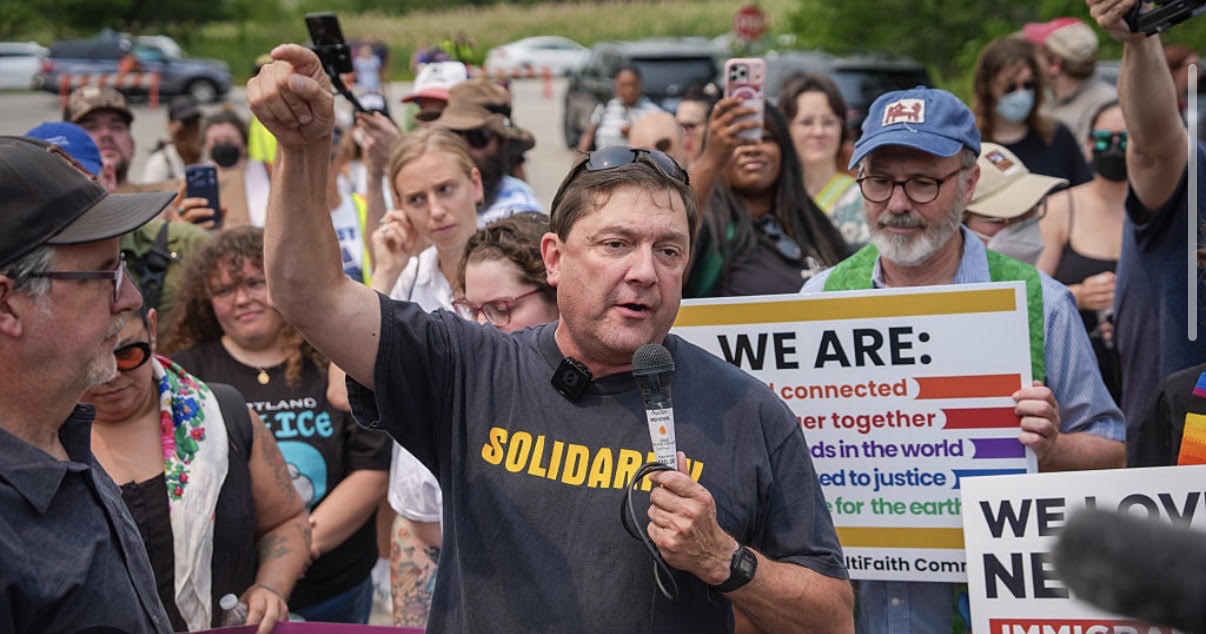 Photo showing Troy Jackson standing outdoors next to a house and stacked wood, wearing a shirt that says SOLIDARITY.