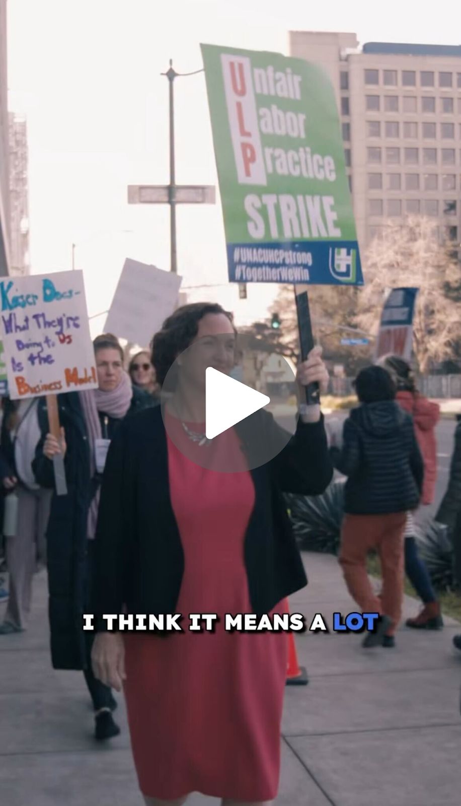 A screenshot from a video of Katie Porter marching on a picket line while holding a sign that says 'Unfair Labor Practice STRIKE'. A caption reads 'I think it means a lot'.
