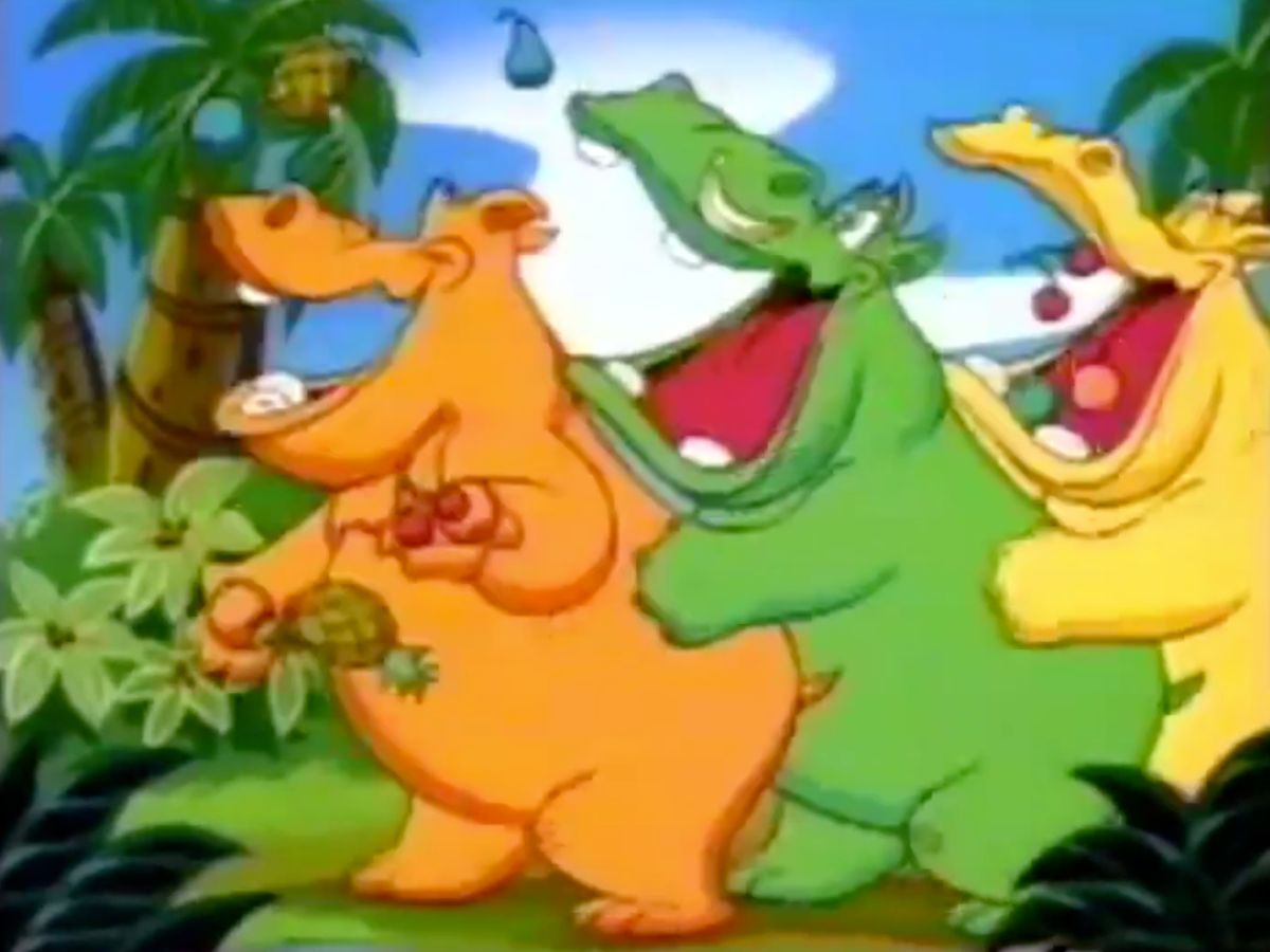 A screenshot from a Hungry Hungry Hippos TV ad showing three colorful cartoon hippos dancing and catching fruit in their mouths.