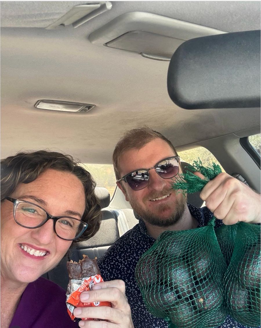A selfie of Katie Porter in a car holding a squashed protein bar, sitting next to a person holding a bag of avocados