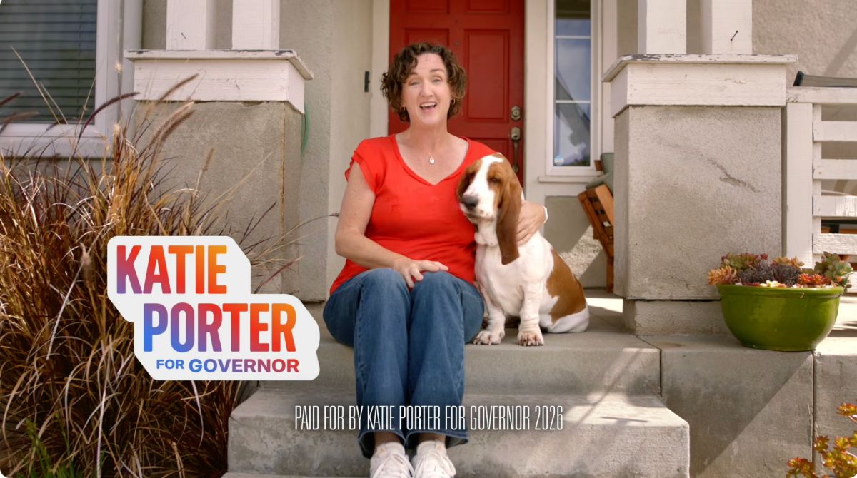 Still from Katie's ad; Katie smiling on a staircase holding her basset hound Poppy; 'Katie Porter For Governor' on the left side of the screen in bold gradient text, 'PAID FOR BY KATIE PORTER FOR GOVERNOR 2026' at the bottom of the screen in white text