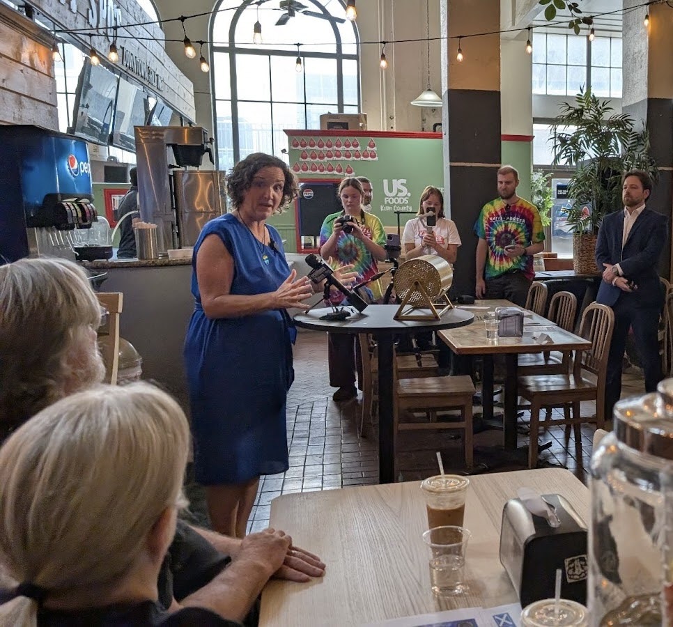 Katie Porter speaking into a microphone in a restaurant on her Whiteboard Warriors tour.