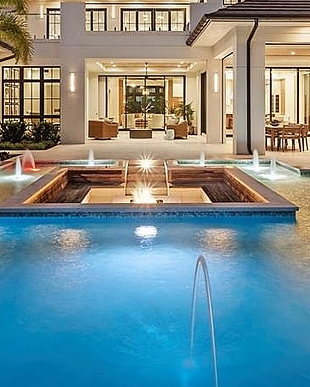 Lit pool and terrace in front of a Mediterranean estate, with uplit citrus trees below
