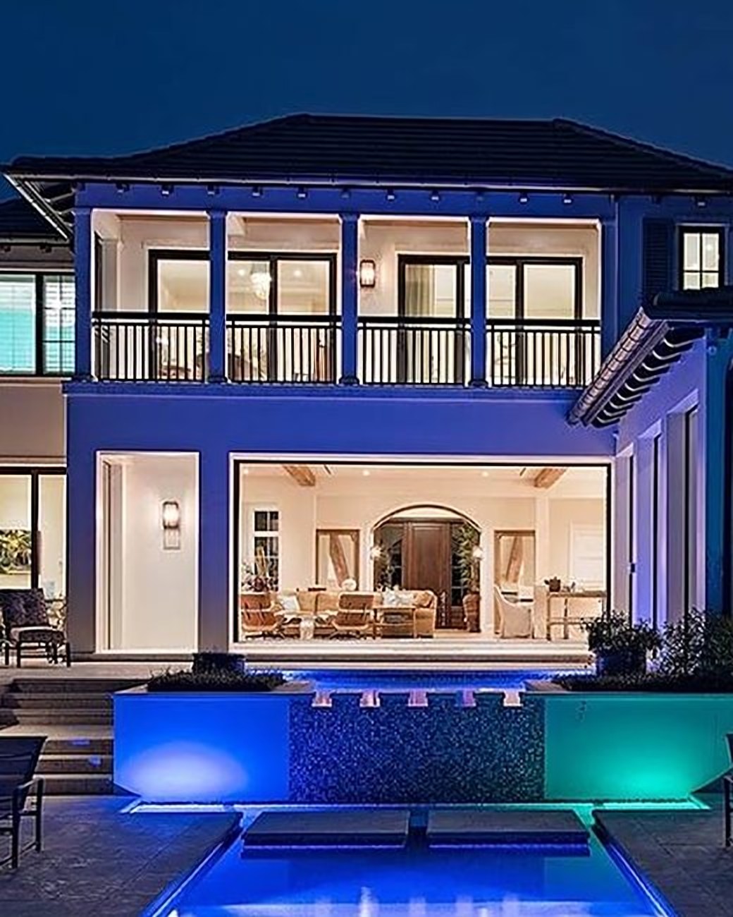 Front elevation of a two-story estate glowing at dusk, with the pool in the foreground