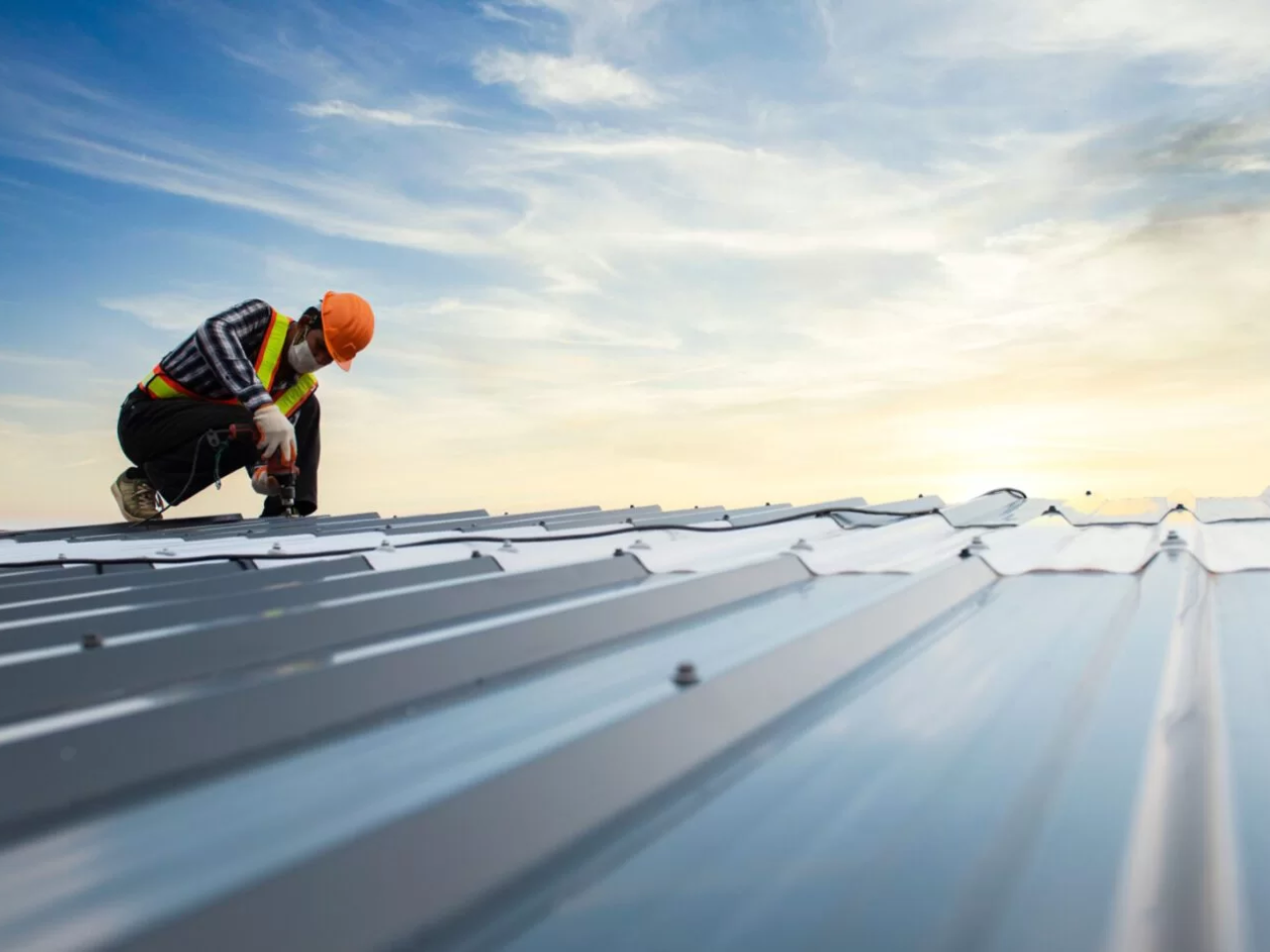 Construction worker installing a metal roof at sunset