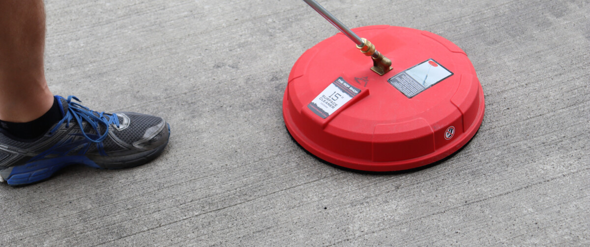 A person using a pressure washer surface cleaner