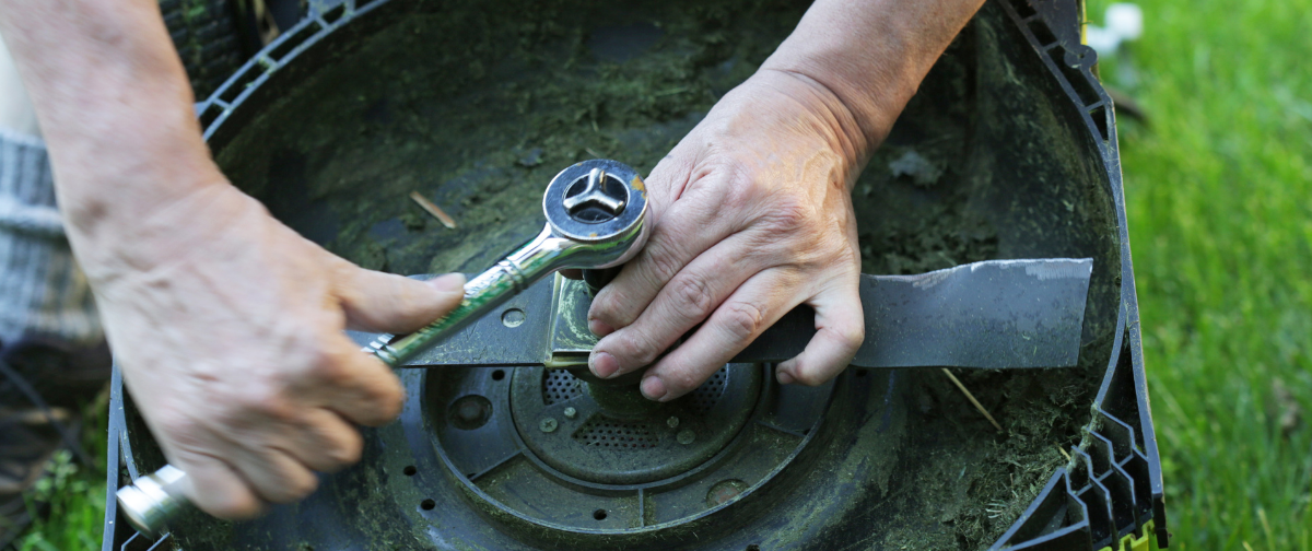 A man uses a wrench to remove a mower blade