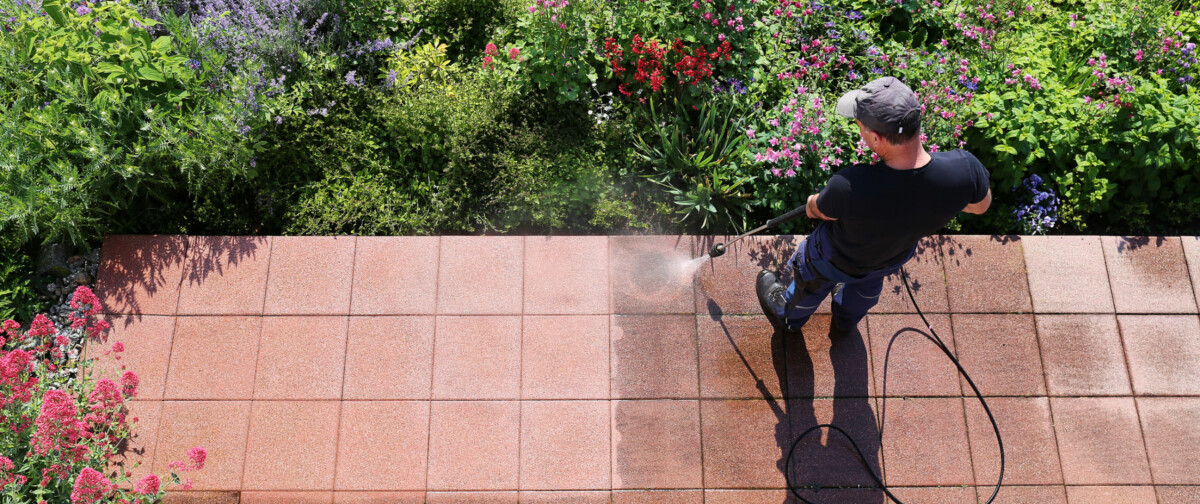 A man uses a pressure washer to clean a patio