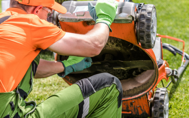 A man does maintenance on the underside of his mower deck