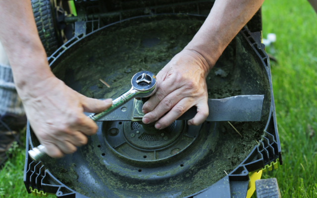 A man uses a wrench to remove a mower blade