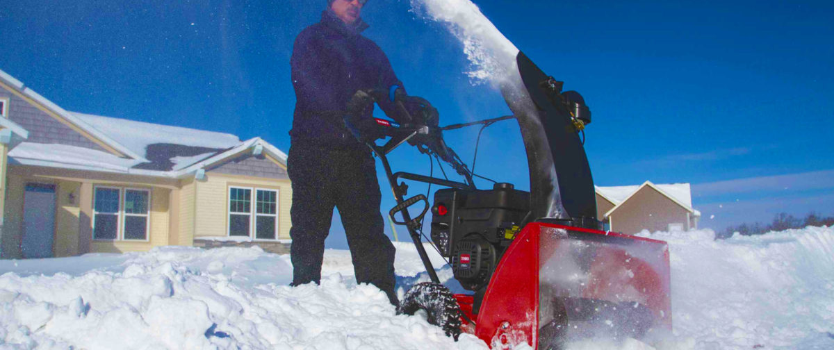 A man clearing a path through snow with his snowthrower.