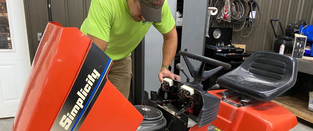A man working on a riding lawnmower.