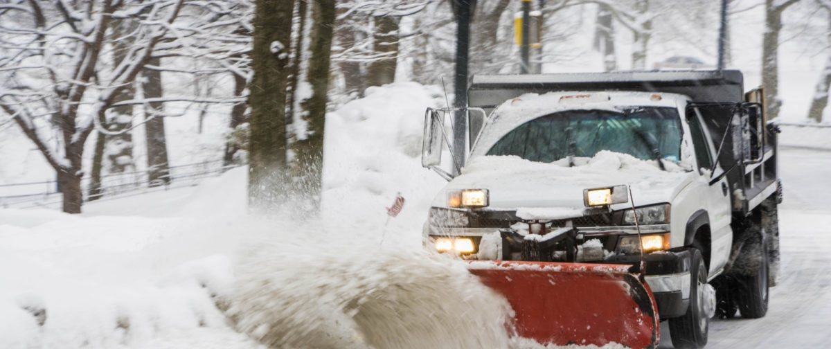 A truck pushing snow to the side on a snowy road.