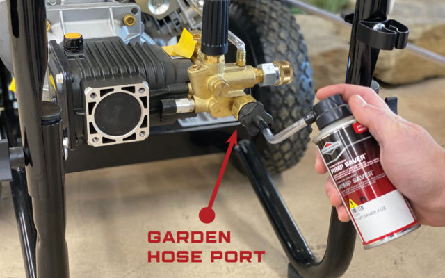 A hand spraying pump saver into the pump of a pressure washer.