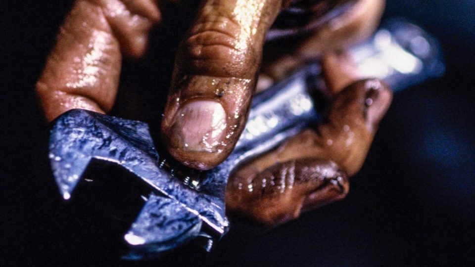 A greasy dirty hand holding an adjustable wrench.