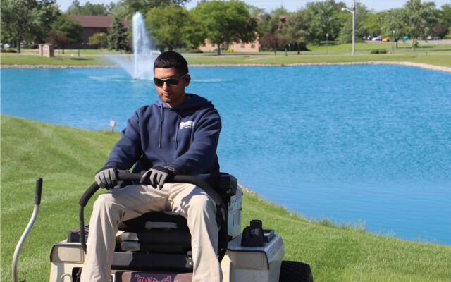 A man on a zero-turn mower near a pond