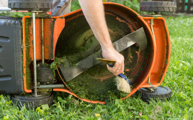 A man cleaning the underside of a push lawnmower deck