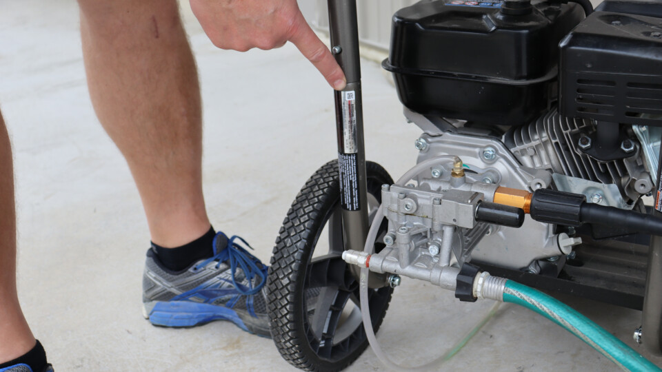 A person pointing to the serial number sticker on a pressure washer