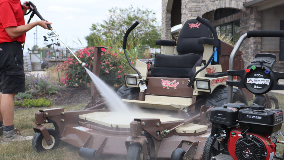 A man pressure washing a mower deck