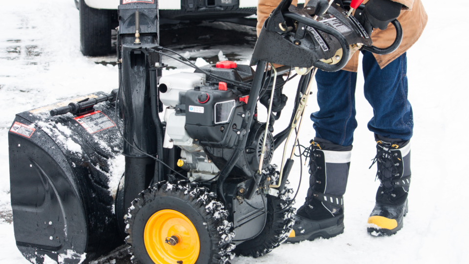 A person leaning over a snowblower outside