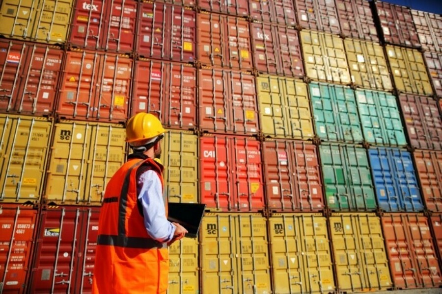 Worker in a hard hat standing by stacks of shipping containers