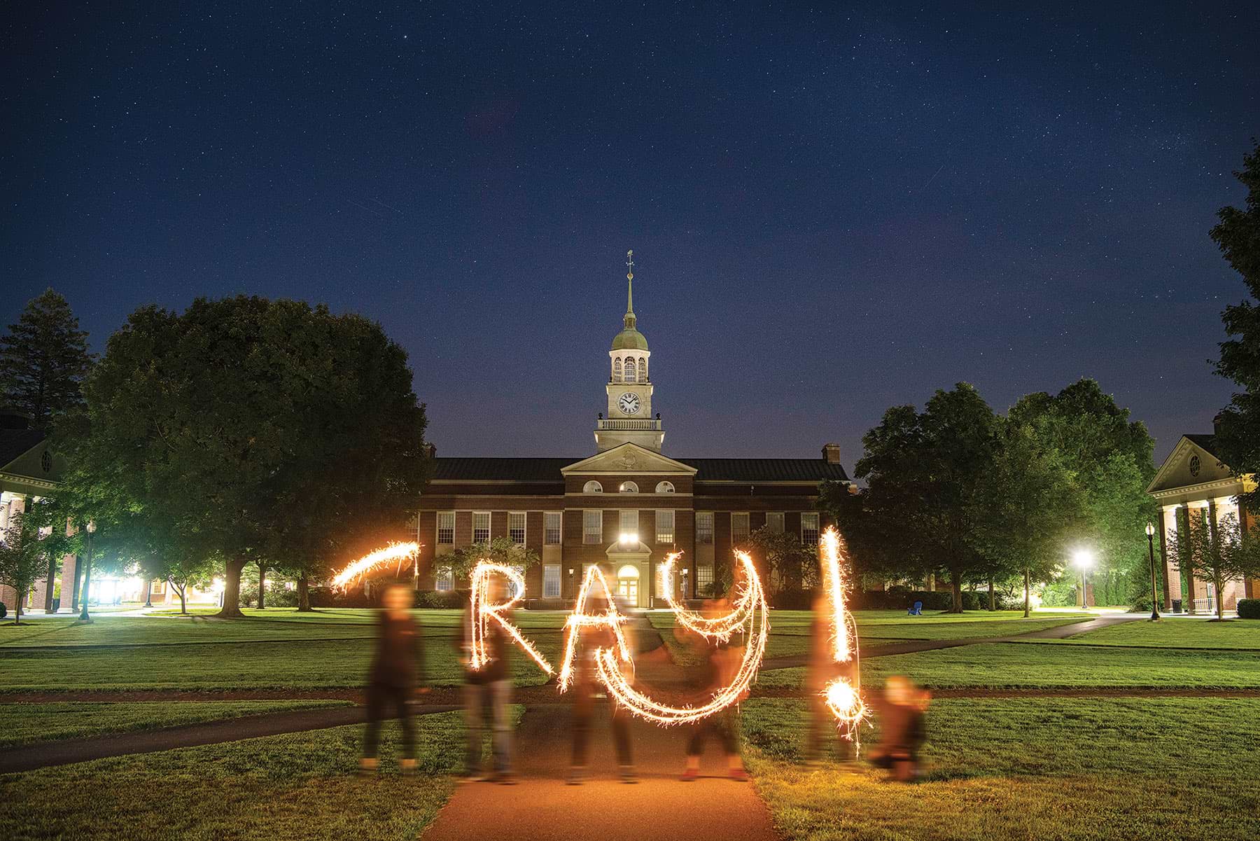 Students writing 'ray with light at night on campus Students writing 'ray with light at night on campus