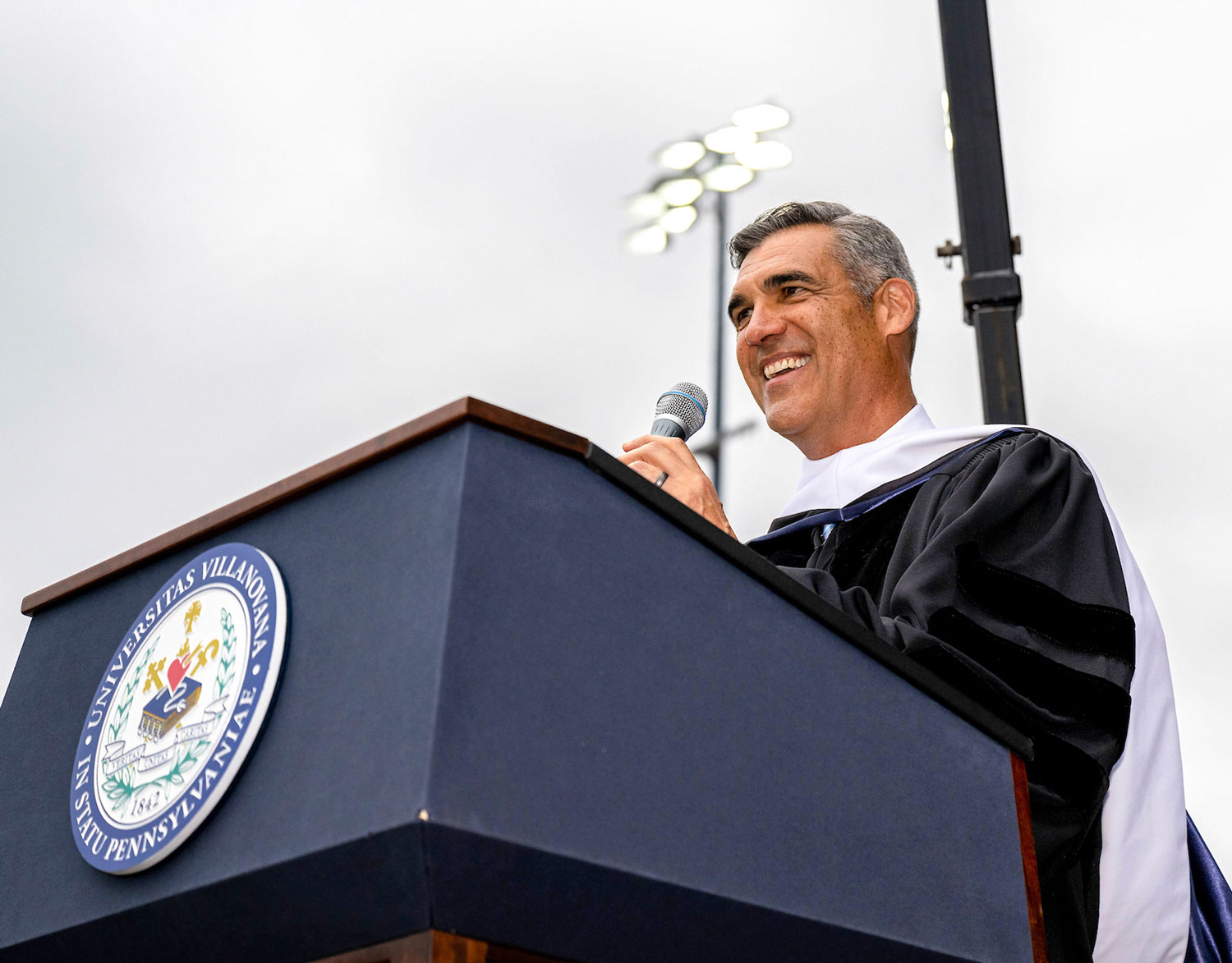 Leaving Their Mark alumni speaker Jay Wright speaks into a podium microphone at an outdoor university event