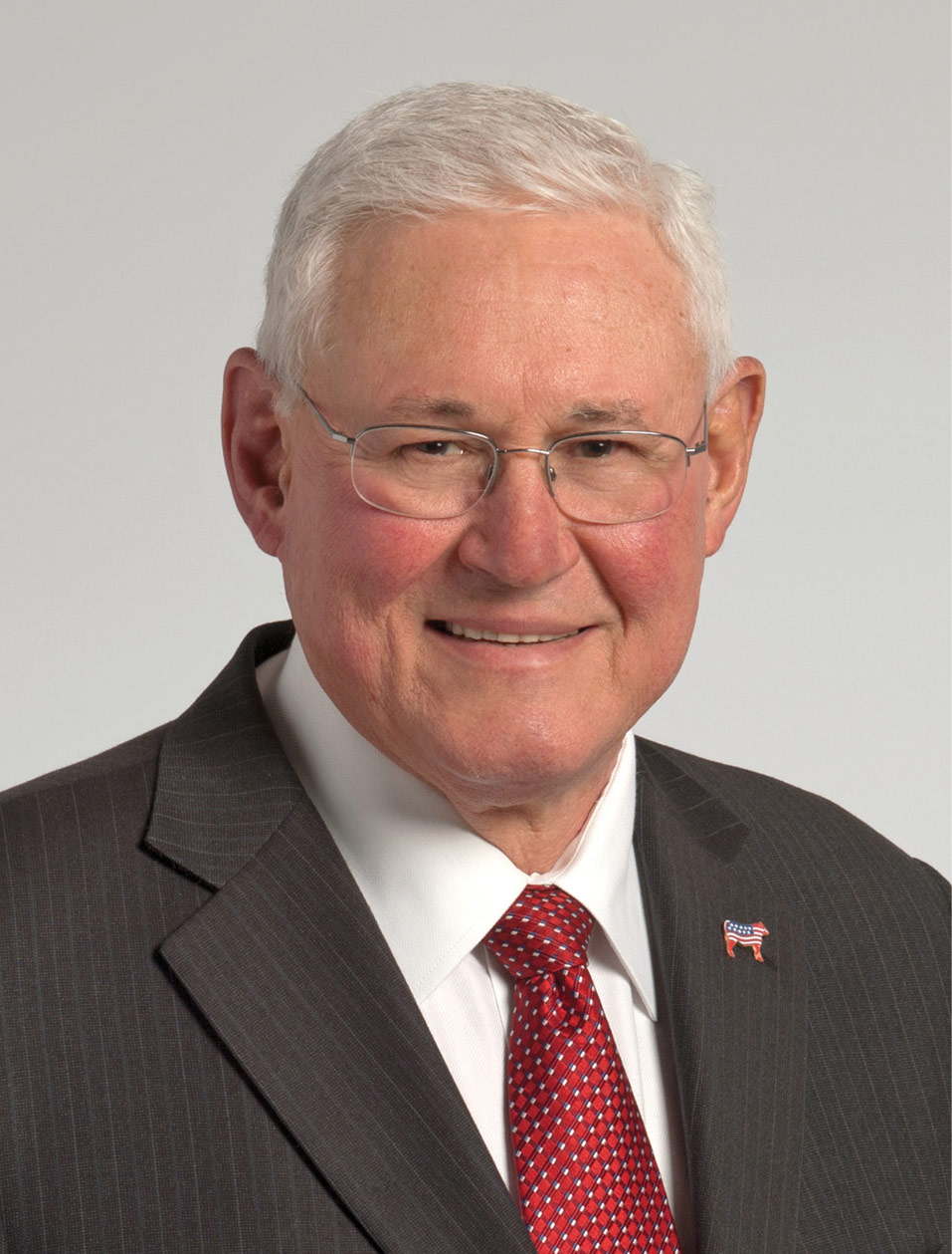 John Bergfeld smiling in dark gray suit with red tie and lapel pin