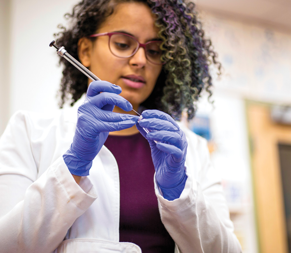 Mona Mohammed in a lab using a syringe while wearing latex gloves