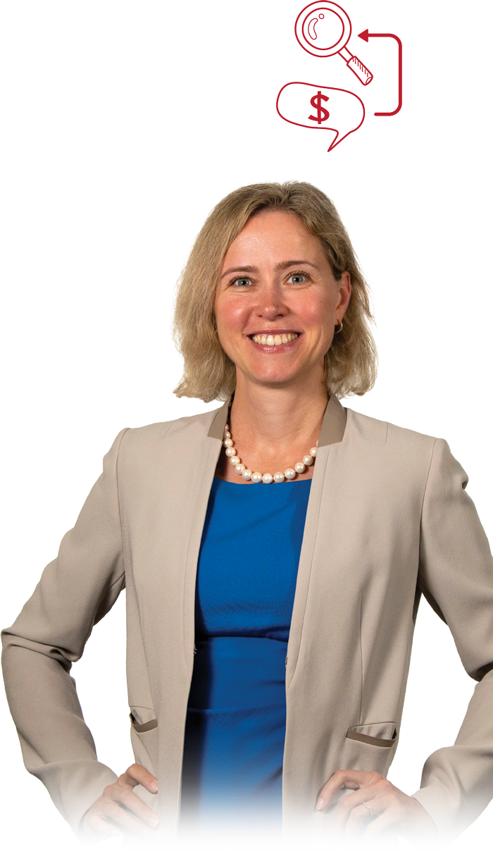 Kate Suslava in a tan jacket and blue dress with hands on her hips and smiling