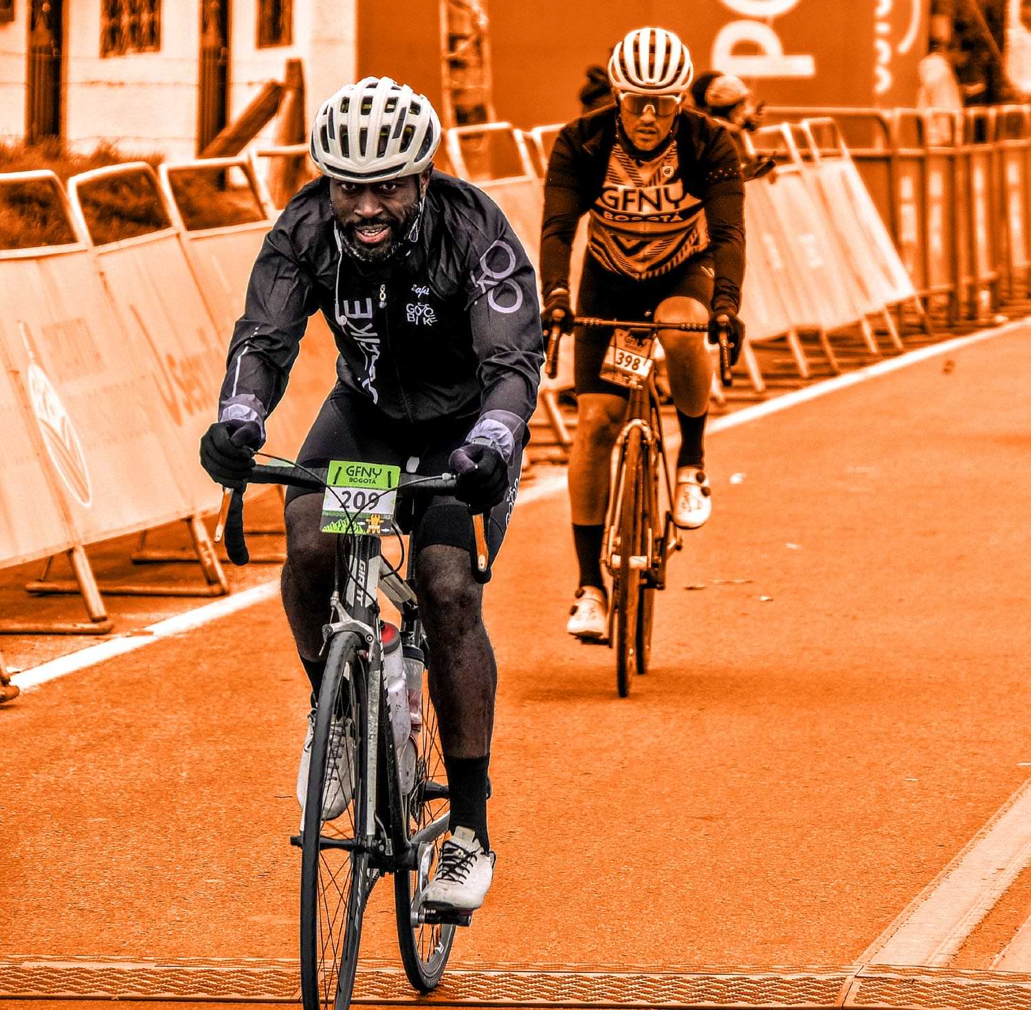 a treated image of Muyambi Muyambi riding a cylcing in full color the setting, along with a cycler at Muyambi's rear are masked in orange