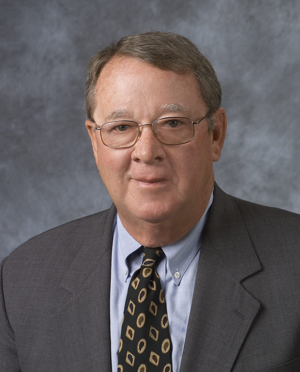 Close-up portrait headshot photograph perspective of Arthur Kinney Jr. '56, P'81 in a dark grey business suit and light sky blue button-up dress shirt with a pattern colored tie (dark navy blue/dark brown)