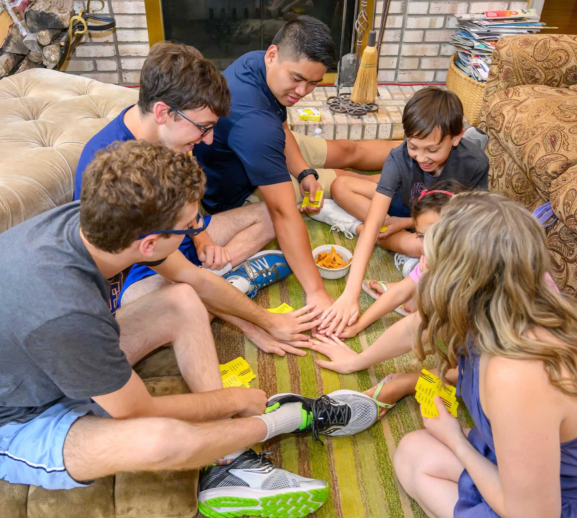 members of the Gale and Agostini families sit in a on a living room floor together playing a card game