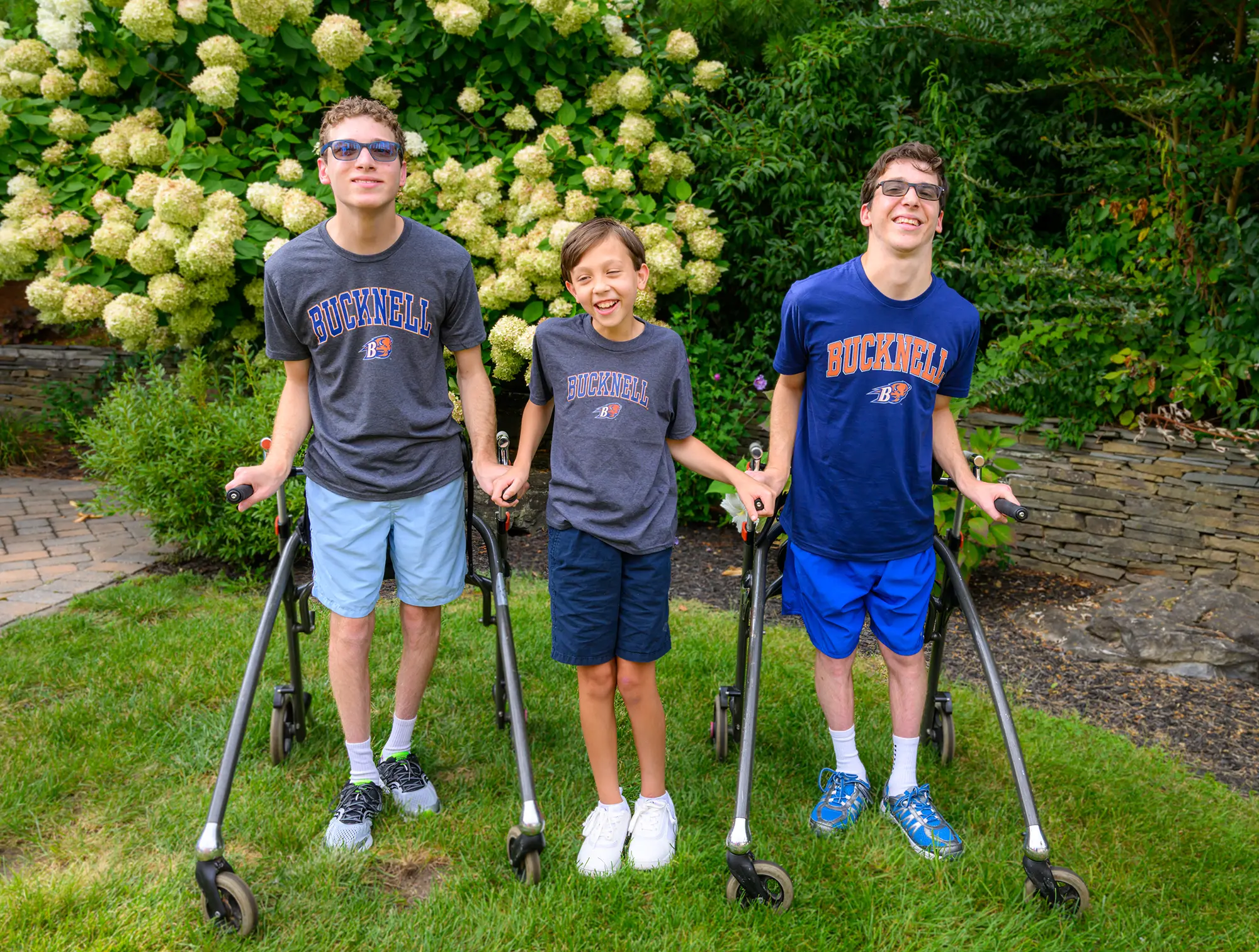 Preston Gale smiles while standing between Matthew and Christian Agostini, both using gait trainers and all three wearing Bucknell t-shirts