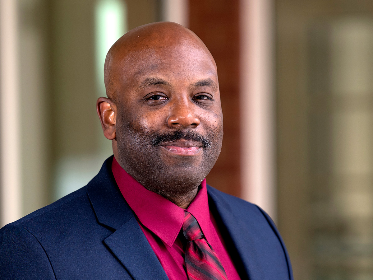 Headshot of Anthony Morgan in a blue suit with a bright pink shirt