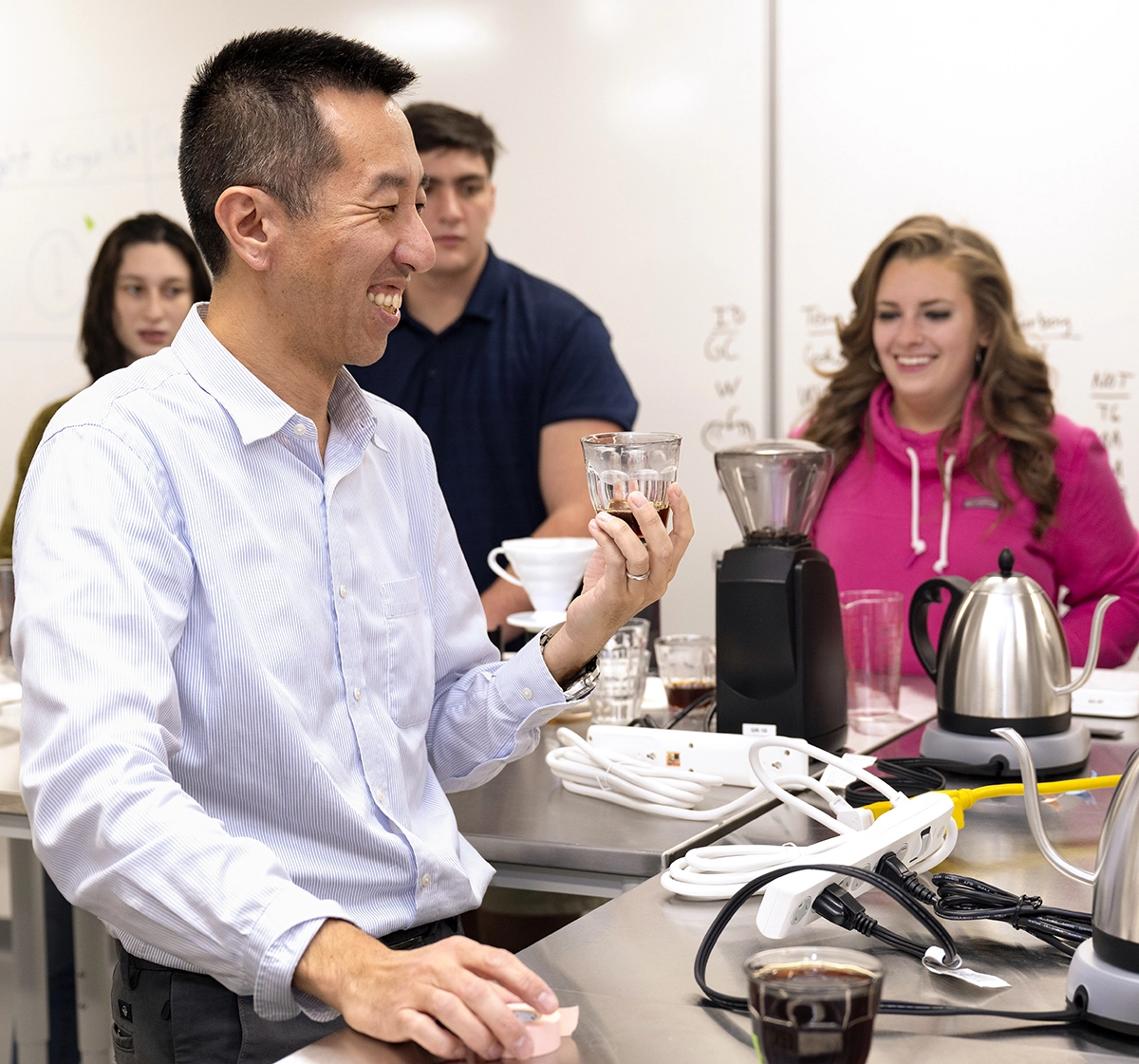 Professor Kat Wakabayashi holding up a glass of coffee and smiling