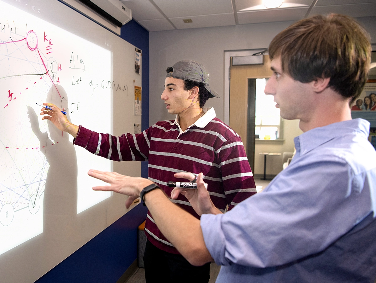 Two students working out a problem written on whiteboard