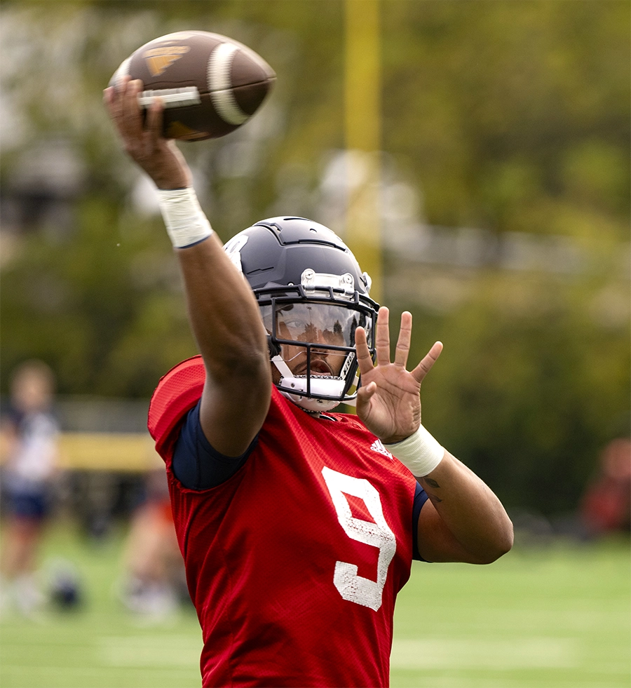 Michael Hardyway wearing a helmet and shoulder pads while throwing a football