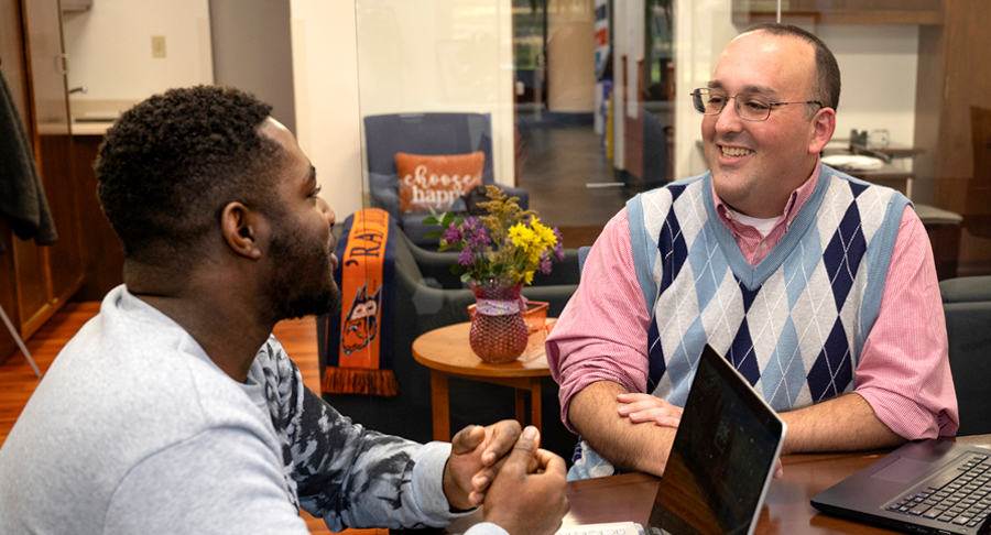 two men smiling and speaking at table with laptops