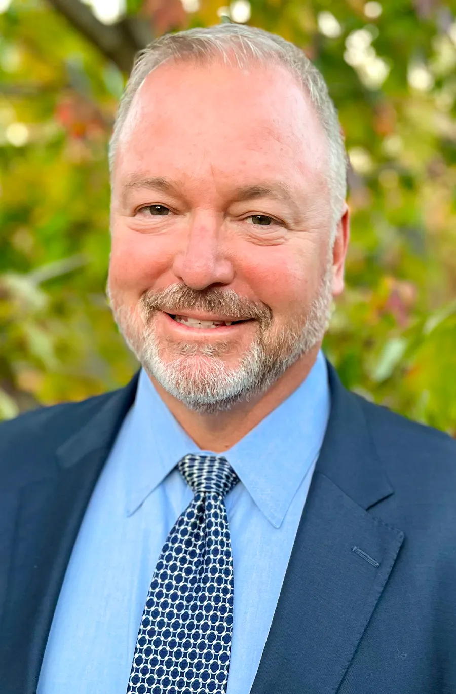 headshot of Wayne Hettenbach ’90 wearing a dark blue patterned tie, a light blue button up shirt and a dark blue suit jacket