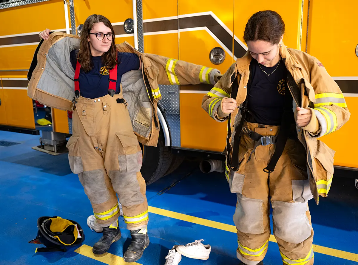 Danielle Kuck ’27 and Isabel Byrnes ’27 put on bunker gear in a fire station