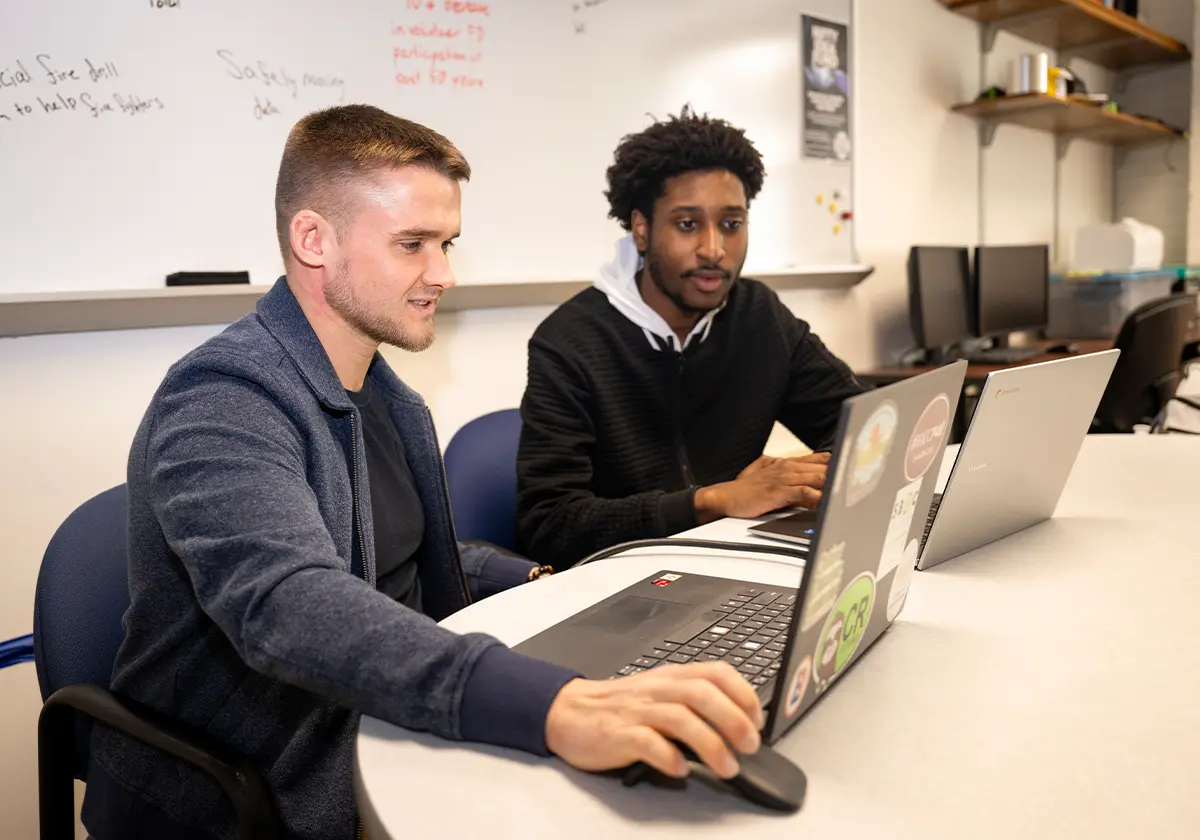 Alec Sanders (left) and Donovan Coleman sit at a table, each with a laptop, in an instruction room