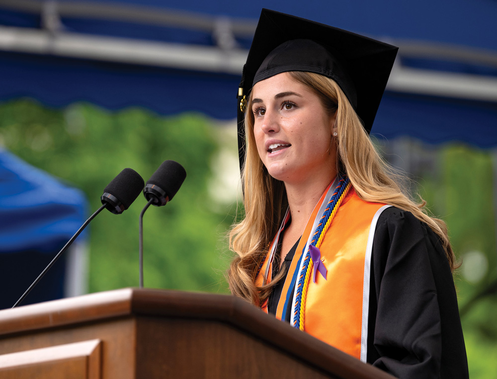 Lea Tarzy giving a speech at a podium in cap and gown